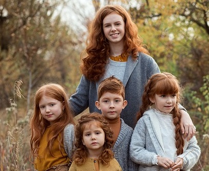 Ein Foto einer jungen Frau, die vier Kinder im Arm hält. Alle haben rote Haare.